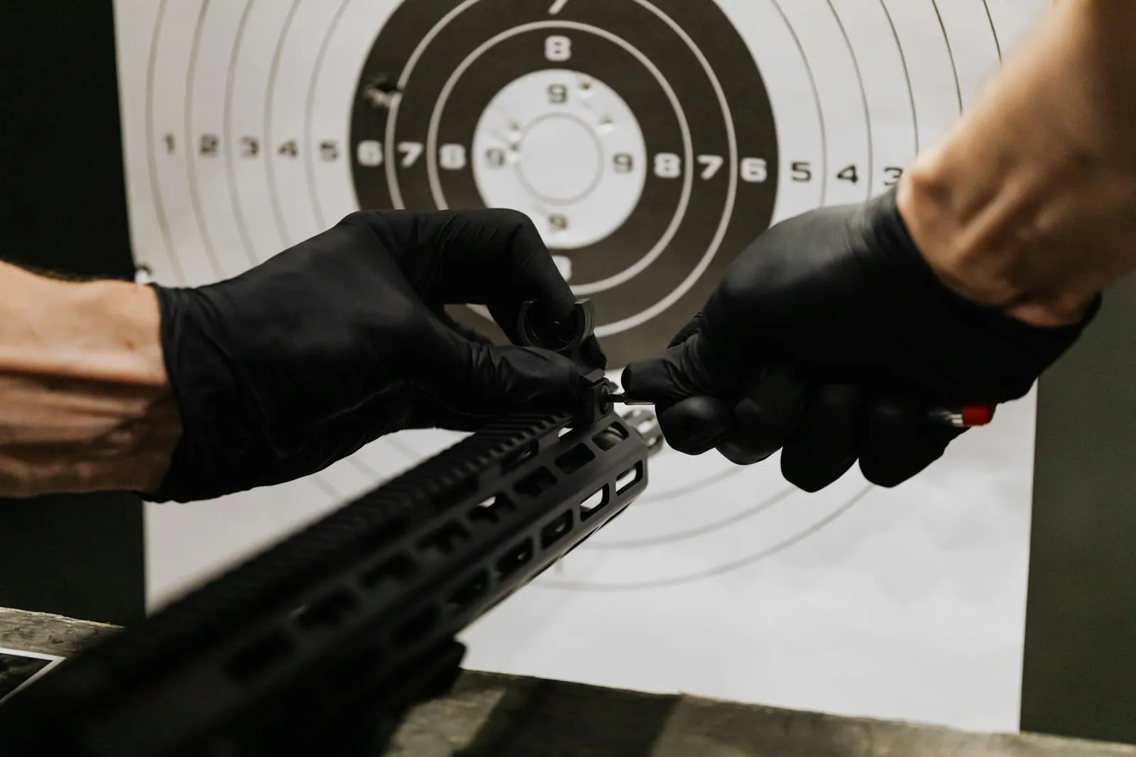 Gloved hands installing a red dot optic on an AR-15 rail at a shooting range